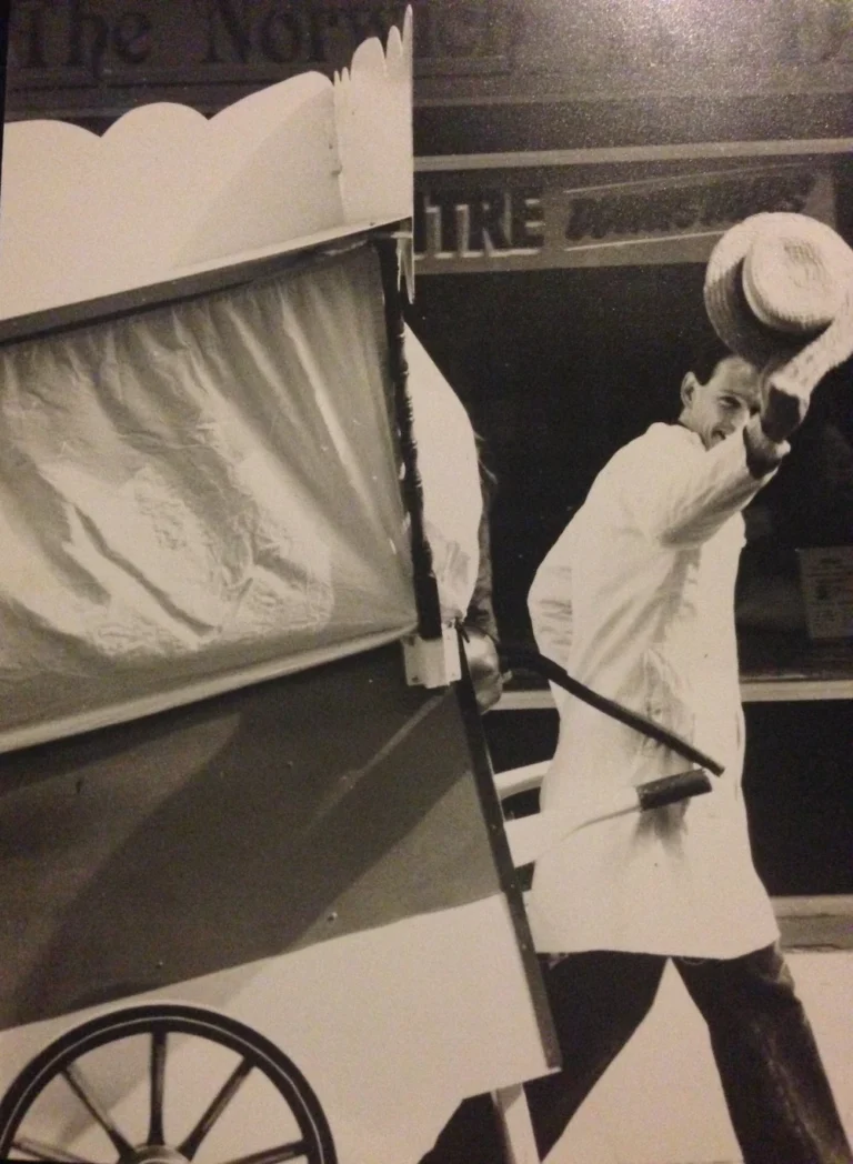 Man pulling cart in traditional attire, waving hat.